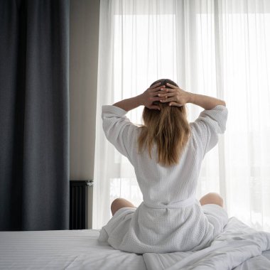 Woman in white bathrobe lying on sofa and relaxing with at home near window