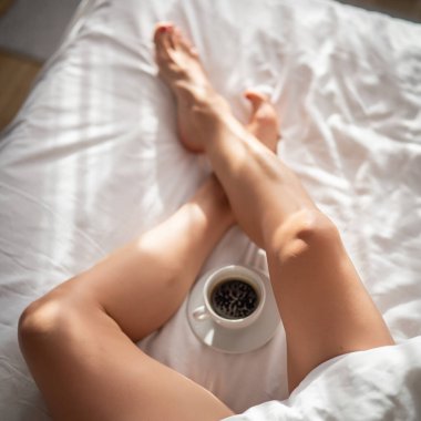 Yatakta bir fincan kahveyle kadın bacaklarına yakın çekim. Otel