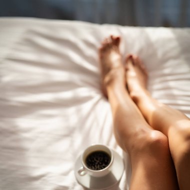 Yatakta bir fincan kahveyle kadın bacaklarına yakın çekim. Otel