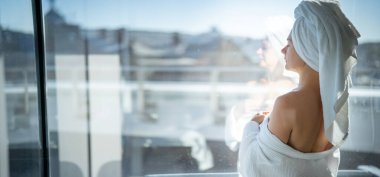 Kafasında havluyla otelin penceresinden dışarı bakan genç bir kadın.