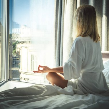 Havluyla yatakta oturup meditasyon yapan genç bir kadın.