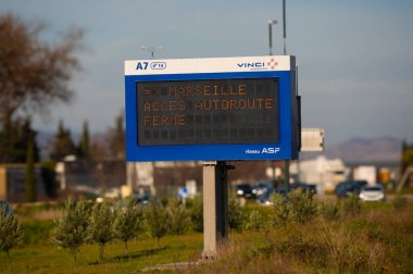 Otoyoldaki elektronik trafik levhası gerçek zamanlı verileri gösteriyor, sürücüleri yönlendiriyor, arkasında arabalar ve ağaçlar var.