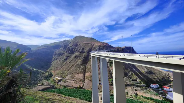 Engebeli dağların nefes kesen manzarası bir yol köprüsü ile berrak mavi gökyüzünün altında ince bulutlarla.