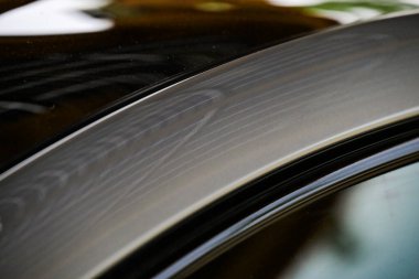 Arabanın sunroof 'undaki su damlacıkları güneş ışığı altında yansıtıcı bir desen oluşturur, parlak ve modern tasarımı vurgular.