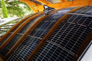 Ahşap bir gölgeliğin altındaki bir arabanın çatısındaki güneş panelleri, taşımacılık için yenilenebilir enerji çözümünü temsil ediyor.