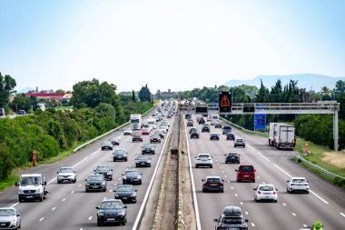 Güneşli bir günde, çevresi yeşilliklerle çevrili yoğun trafik gösteren araba ve kamyonlarla dolu otoyol..