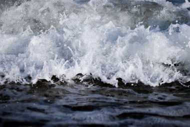 Dalgalı köpüklü deniz suyunun yüzeyi, yakın çekim. Sığ alan derinliği.