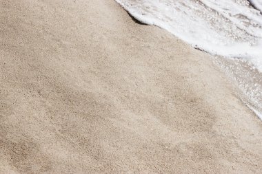 Sahilde köpüklü okyanus dalgalarıyla kumlara yakın çekim. Pankartlar için metin kopyalama alanı