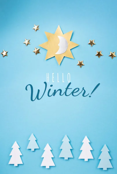Hello Winter Blue Card Concept. Sun, moon, golden stars and winter forest symbol on blue paper background.  Flat lay, top view, copy space. Winter solstice day holiday, December 21.