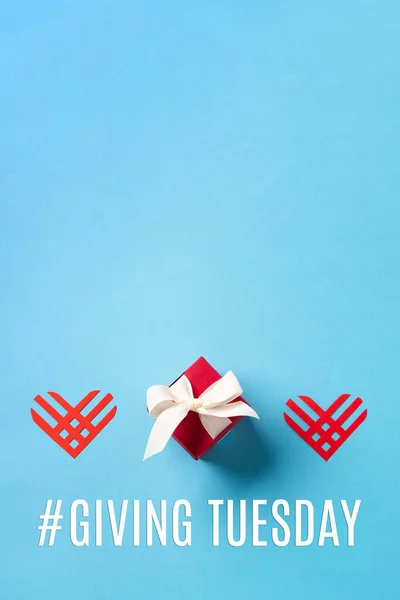 Giving Tuesday, global day of charitable giving after Black Friday shopping day. Charity, give help, donations support concept. Red paper hearts and gift box on blue background. Top view, copy space.