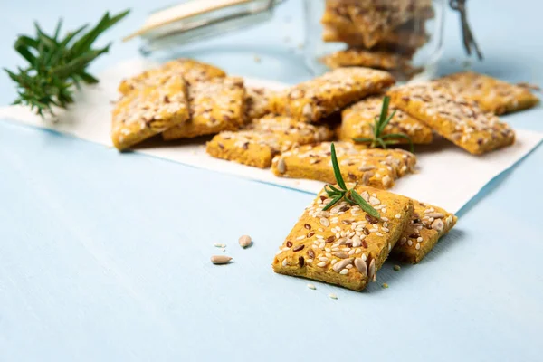 Gluten free Homemade Crackers and rosemary on Blue background. Healthy eating, ancient grain food, dieting, balanced food concept. Cereals gluten-free, millet, quinoa, flax seeds, sunflower seeds.