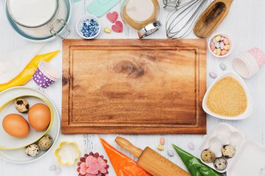 Paskalya için tatlı pişirme konsepti. Hamur, yumurta, merdane, çırpma fırçası, kurabiye keskisi, şeker serpiştirme, un. Rustik beyaz tahta arkaplan, üst görünüm kopyalama alanı.