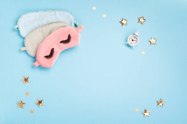 World Sleep day observed on March. Quality of sleep, good night, insomnia, relaxation concept. Sleeping masks, golden stars and white alarm clock on blue background. Flat lay, top view