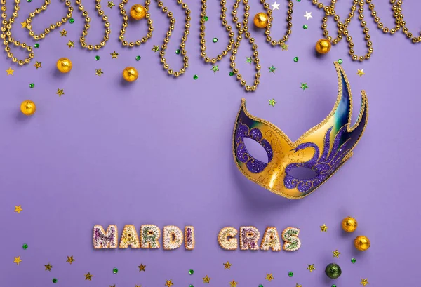 Mardi Gras King Cake cookies, masquerade festival carnival mask, gold beads and golden, green confetti on purple background. Holiday party invitation, greeting card concept.
