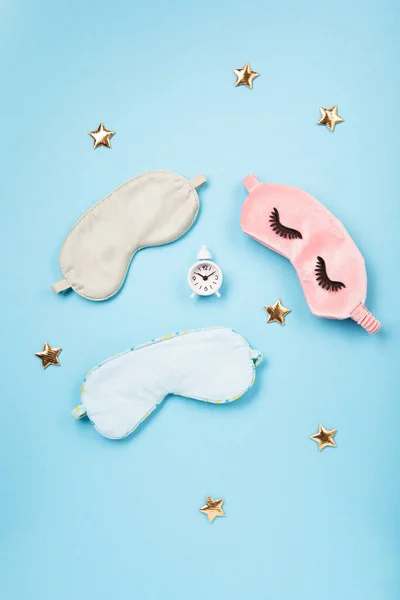 World Sleep day observed on March. Quality of sleep, good night, insomnia, relaxation concept. Sleeping masks, golden stars and white alarm clock on blue background. Flat lay, top view