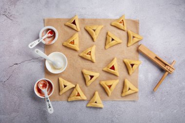 Making homemade Triangular pastry, Hamantaschen cookies for Purim. Purim celebration, jewish carnival holiday concept. Dough, jam, sugar, butter and rolling pin on gray stone table. Top view, flat lay, copy space.