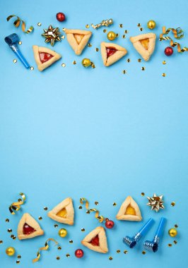 Purim celebration jewish carnival holiday concept. Tasty hamantaschen cookies, Carnival mask, noisemaker, sweet candies and party decor on blue background. Top view, flat lay, copy space. clipart