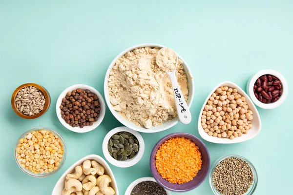 Plant based protein food (legumes, lentils, beans, seeds) and Healthy dry Pea Protein Powder, food supplement, Fitness nutrition on blue green background. Vegan, vegetarian food concept.