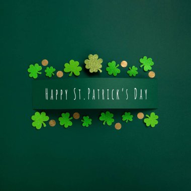 St. Patrick's Day celebration Concept. Greeting card with traditional symbols - Golden horseshoe, gold coins and clover leaves, green shamrocks on green background. Top view, copy space.
