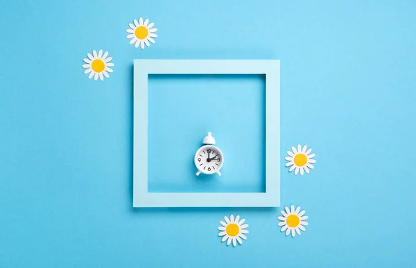 White alarm clock and Daisy Flowers on blue background. Spring forward, Time Change, Daylight Saving Time Ends, Changing the time on the watch to spring time, Summer back concept.