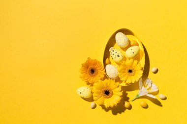 Bayramlık Paskalya kompozisyonu. Sarı, pembe ve beyaz paskalya yumurtaları, sarı kağıtta papatya çiçekleri. Bahar Paskalya kartı konsepti. Düz konum, üst görünüm, kopyalama alanı.