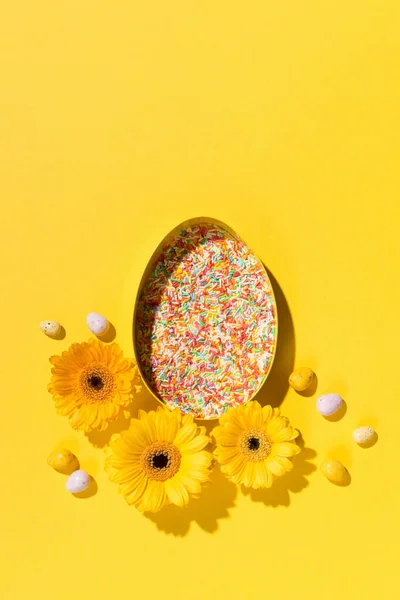 Festive holiday Easter composition. Yellow, pink, blue and white sugar sprinkles and sweet Easter eggs on paper yellow background. Spring Easter card concept. Flat lay, top view, copy space.