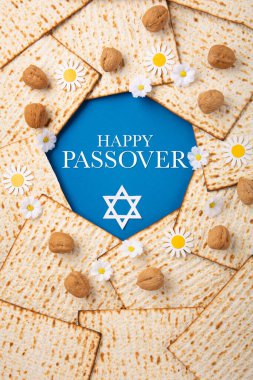 Jewish holiday Passover greeting card concept with matzah, nuts, spring flowers on blue table. Seder Pesach spring holiday background, top view, copy space.