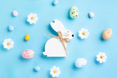 Sweet Colorful Easter Eggs, white  Easter Bunny, daisy flowers on pastel blue background. Happy Easter greeting card concept. Flat lay, top view, copy space.