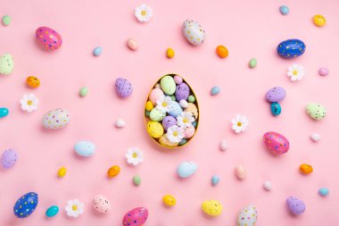 Sweet Colorful Easter Eggs and spring white daisy flowers on pastel pink background. Happy Easter greeting card concept. Flat lay, top view, copy space.