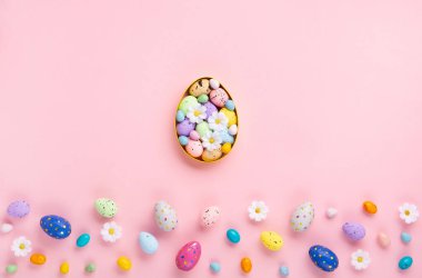 Sweet Colorful Easter Eggs and spring white daisy flowers on pastel pink background. Happy Easter greeting card concept. Flat lay, top view, copy space.