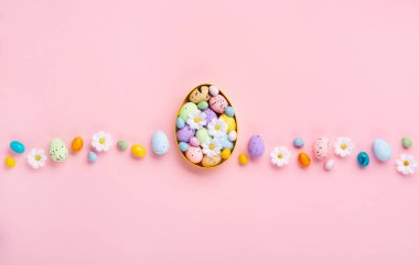 Sweet Colorful Easter Eggs and spring white daisy flowers on pastel pink background. Happy Easter greeting card concept. Flat lay, top view, copy space.