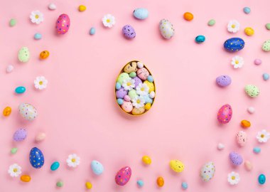 Sweet Colorful Easter Eggs and spring white daisy flowers on pastel pink background. Happy Easter greeting card concept. Flat lay, top view, copy space.