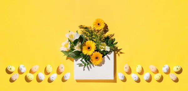 Festive holiday Easter flower composition. Yellow and white flowers, pastel easter eggs on paper yellow background. Spring, Easter card concept. Flat lay, top view, copy space.