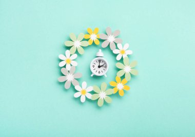 White alarm clock and Daisy Flowers on blue mint background. Spring forward, Time Change, Daylight Saving Time Ends, Changing the time on the watch to spring time, Summer back concept.