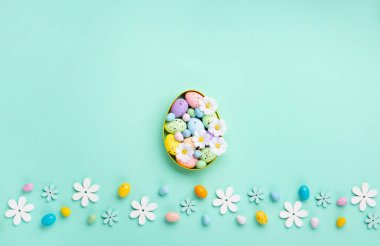 Sweet Colorful Easter Eggs and white daisy flowers on pastel blue background. Happy Easter greeting card concept. Flat lay, top view, copy space.
