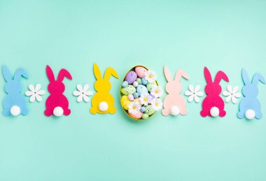 Colorful Easter Bunnies, Sweet Colorful Easter Eggs, daisy flowers on pastel blue mint background. Happy Easter greeting card concept, copy space.
