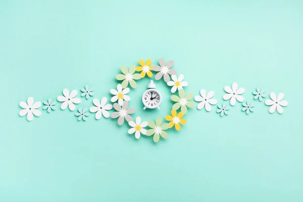 青いミントの背景に白い目覚まし時計とデイジーの花 春の楽しみ 時間の変化 昼間の時間の節約終了 春の時間に時計の時間を変更 夏のバックコンセプト — ストック写真