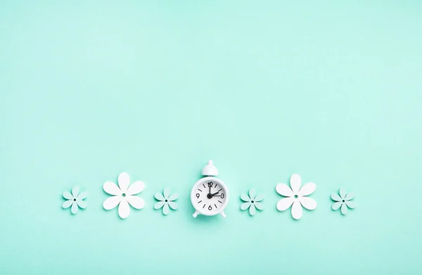 White alarm clock and Daisy Flowers on blue mint background. Spring forward, Time Change, Daylight Saving Time Ends, Changing the time on the watch to spring time, Summer back concept.