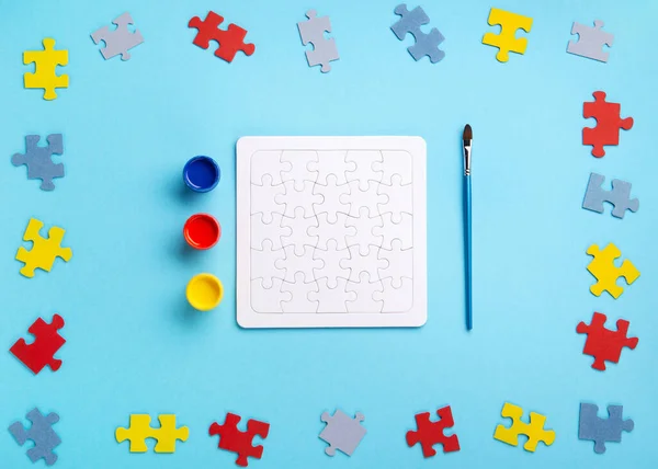 World Autism Awareness Day or month concept. Creative design for April 2. White puzzles, symbol of awareness for autism spectrum disorder and colorful paints on blue background. Top view, copy space.
