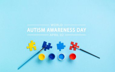 World Autism Awareness Day or month concept. Creative design for April 2. White puzzles, symbol of awareness for autism spectrum disorder and colorful paints on blue background. Top view, copy space.