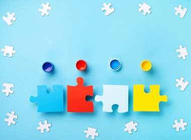 World Autism Awareness Day or month concept. Creative design for April 2. White puzzles, symbol of awareness for autism spectrum disorder and colorful paints on blue background. Top view, copy space.