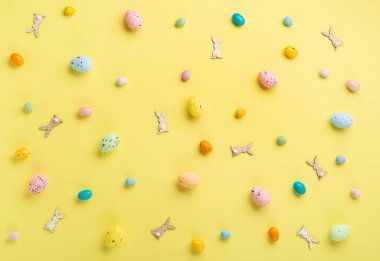 Renkli Paskalya yumurtaları ve pastel sarı arka planda bahar beyaz papatya çiçekleri. Paskalya tebrik kartı konseptin kutlu olsun. Düz konum, üst görünüm, kopyalama alanı.