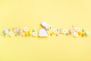 Beyaz ahşap Paskalya Tavşanı, Tatlı Renkli Paskalya Yumurtaları, Pastel sarı arka planda papatya çiçekleri. Mutlu Paskalya tebrik kartı kavramı, kopyalama alanı.