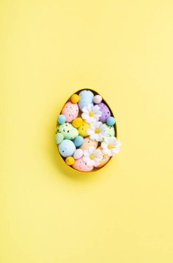 Renkli Paskalya yumurtaları ve pastel sarı arka planda bahar beyaz papatya çiçekleri. Paskalya tebrik kartı konseptin kutlu olsun. Düz konum, üst görünüm, kopyalama alanı.