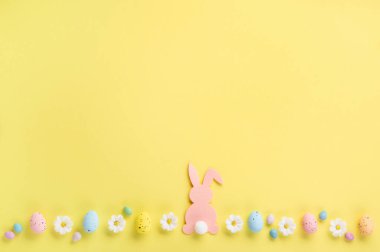 Pembe Paskalya Tavşanı, Tatlı Renkli Paskalya Yumurtaları, Pastel sarı arka planda papatya çiçekleri. Mutlu Paskalya tebrik kartı kavramı, kopyalama alanı.