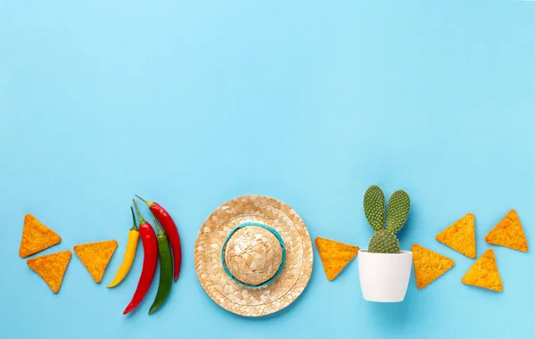 Mexican background fiesta with Traditional Mexican nachos chips, chilli pepper, cactus and sombrero hat on blue background. Cinco de Mayo (Fifth of May) celebration concept. Top view, copy space.