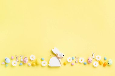 Beyaz ahşap Paskalya Tavşanı, Tatlı Renkli Paskalya Yumurtaları, Pastel sarı arka planda papatya çiçekleri. Mutlu Paskalya tebrik kartı kavramı, kopyalama alanı.