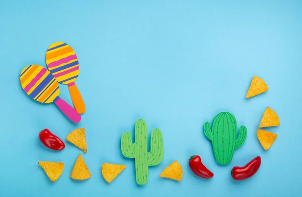 Mexican background fiesta with Traditional Mexican nachos chips, red chilli pepper, cactus and maracas on blue background. Cinco de Mayo (Fifth of May) celebration concept. Top view, copy space.