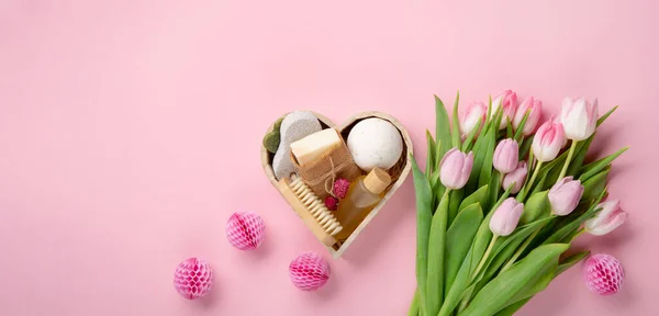 Natural eco friendly beauty skin care products, spa accessories for women and spring tulip flowers on pink background. Zero waste self care heart shape gift box for mothers day, womans day, birthday.