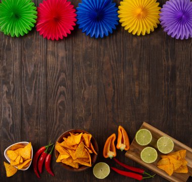 Cinco de Mayo (5 Mayıs) kutlama konsepti. Geleneksel Meksika cipsleriyle Meksika arka plan şenliği, kırmızı biber, koyu ahşap arka planda yeşil limon. Üst görünüm, alanı kopyala.